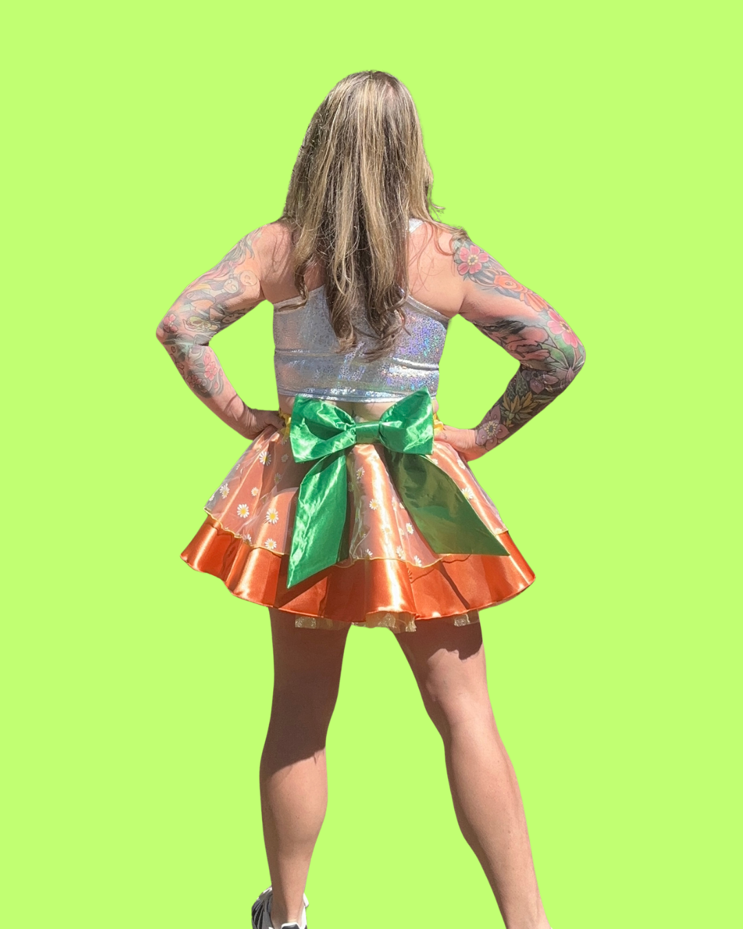 Person wearing a colorful orange bird running tutu skirt with a large green bow on a bright green background