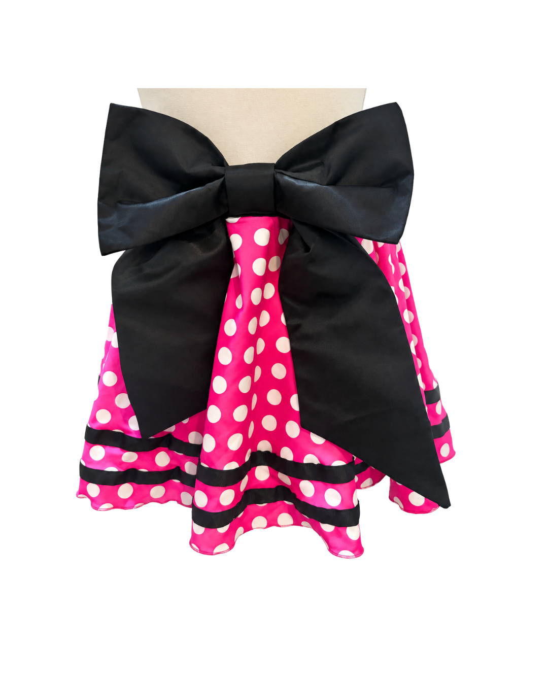 A pink and white polka dot skirt with a large black bow at the waist, displayed on a beige mannequin torso against a white background.
