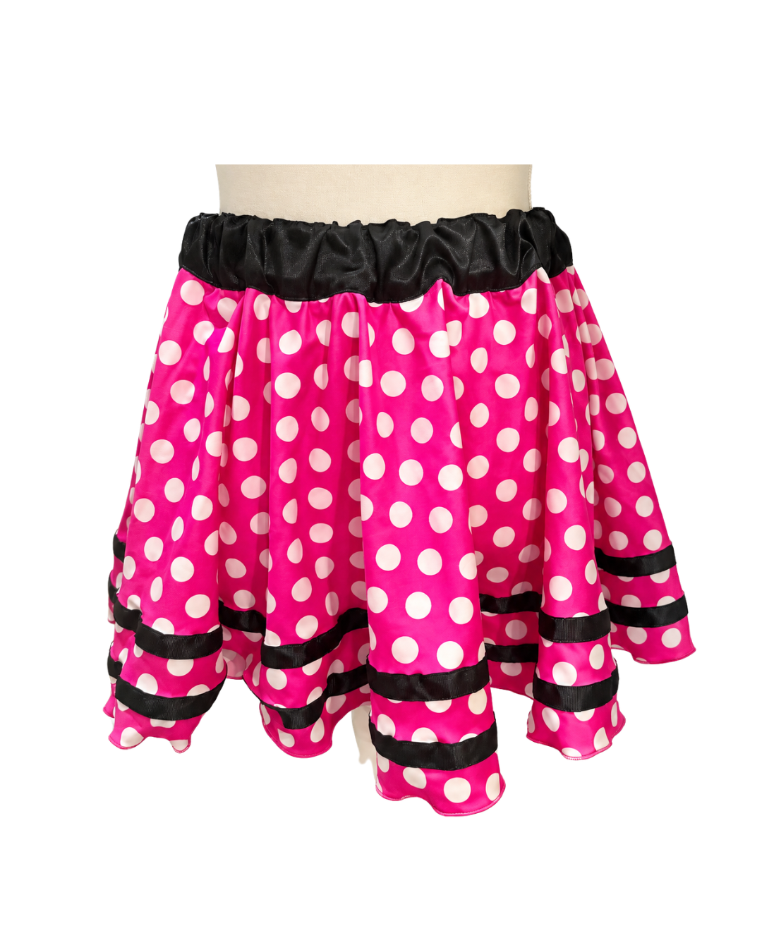 A bright pink skirt with white polka dots and black ruffled trim at the waistband and hem, displayed on a mannequin torso against a white background.