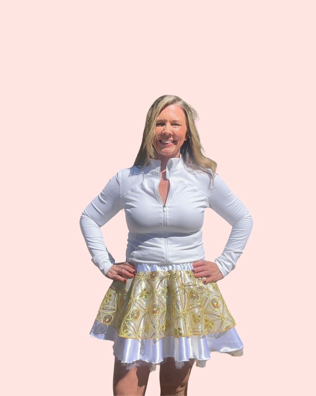Woman wearing a white long-sleeve top and gold skirt on a pink background - running skirt styled after the cake bake