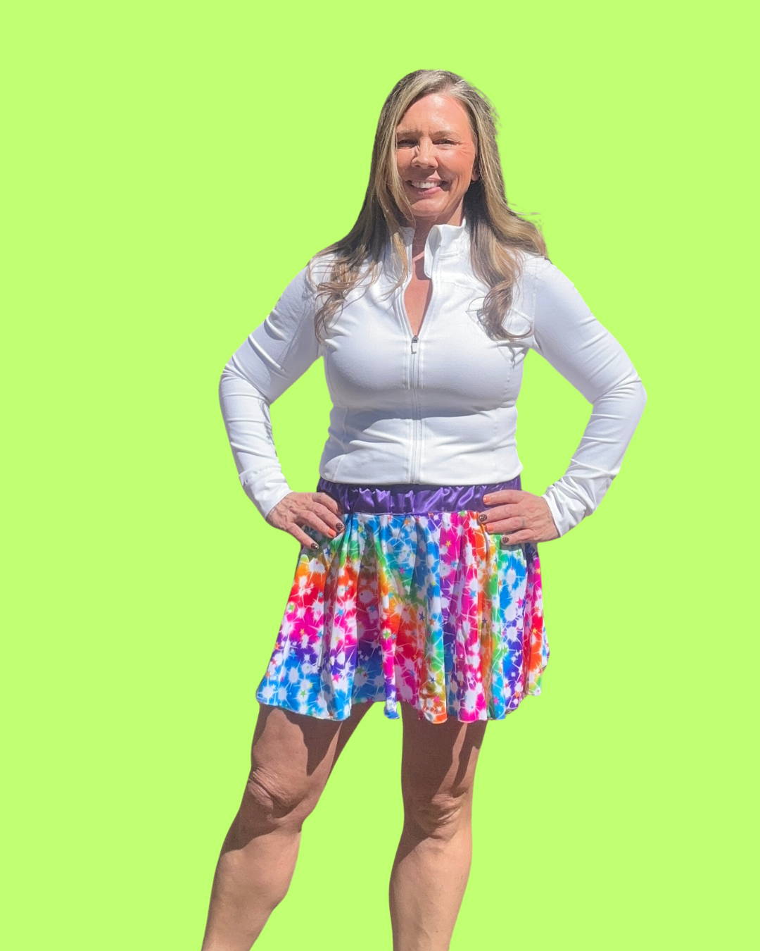 Woman wearing a white long-sleeve top and colorful tie-dye pride running skirt on a green background