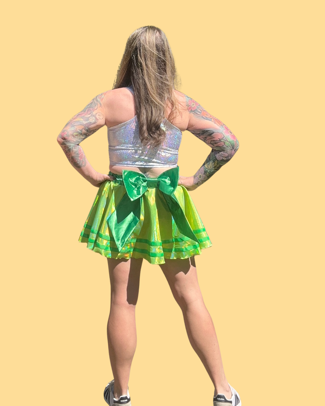 Person wearing a silver top and green running skirt with a bow on a yellow background