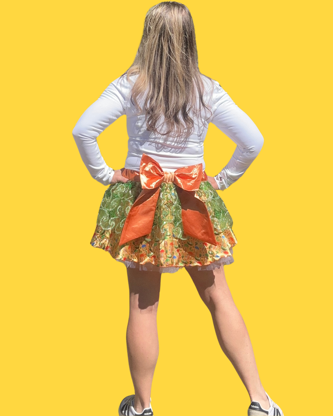 Person wearing a colorfu tiki room running skirt with a large orange bow on a yellow background