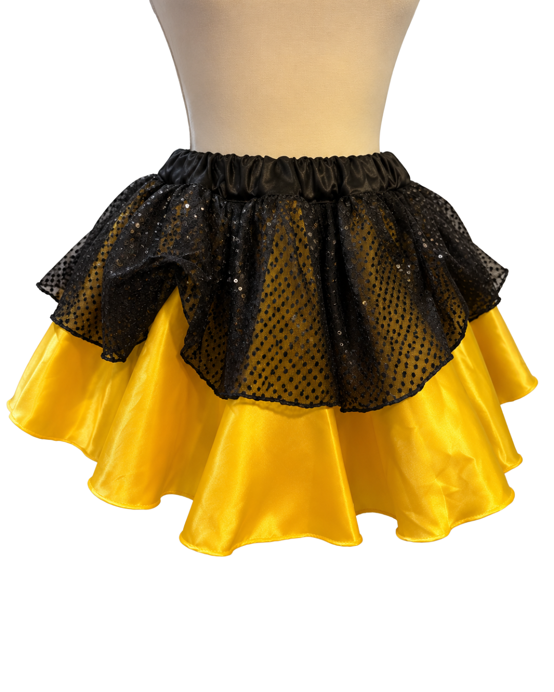 A two-tiered ruffled skirt displayed on a beige mannequin torso against a white background. The top tier is made of black mesh fabric with small sequins, and the bottom tier is made of bright yellow satin-like fabric.